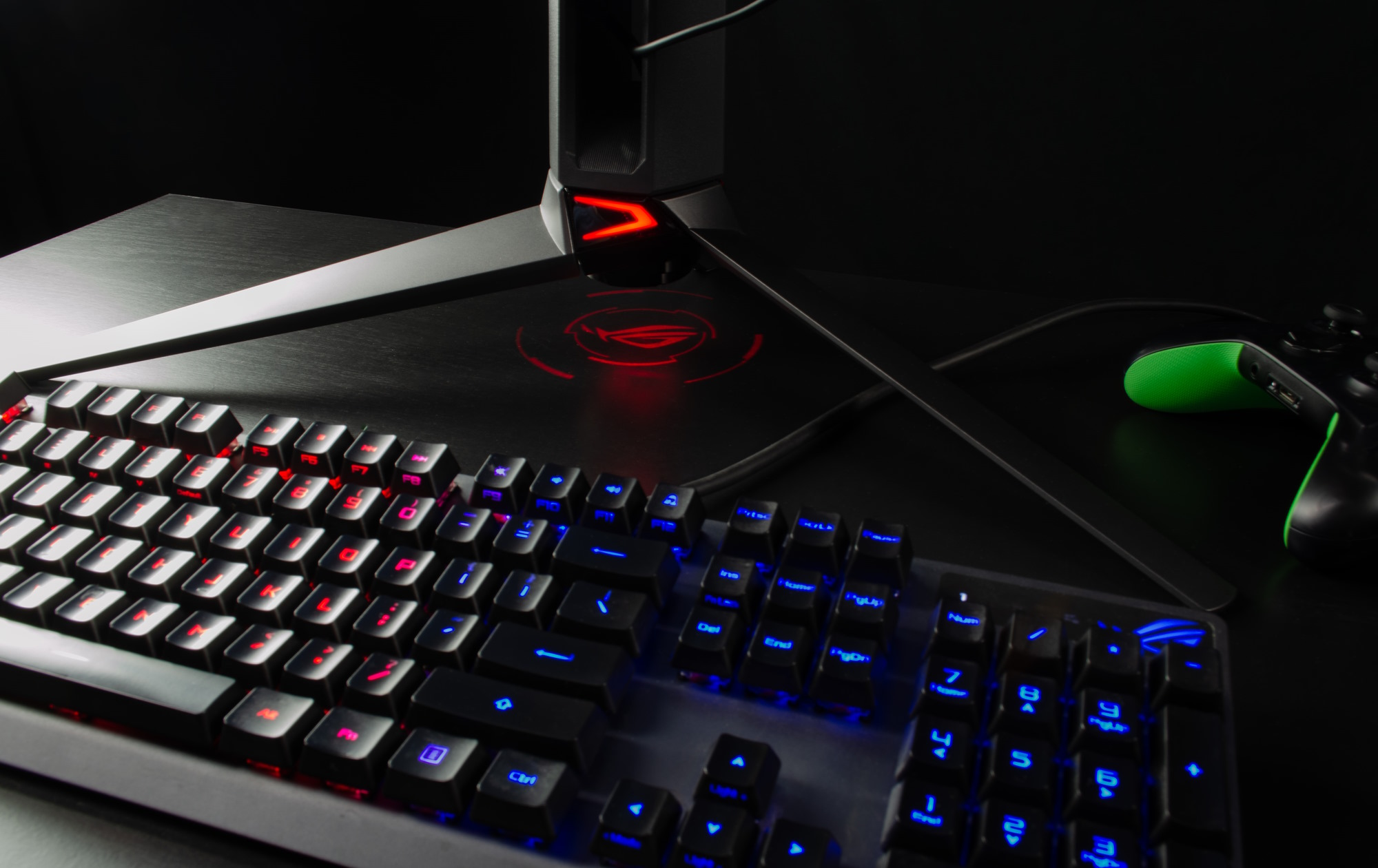 The stand of the PG27AQDM on a desk with an ROG keyboard and an Xbox controller