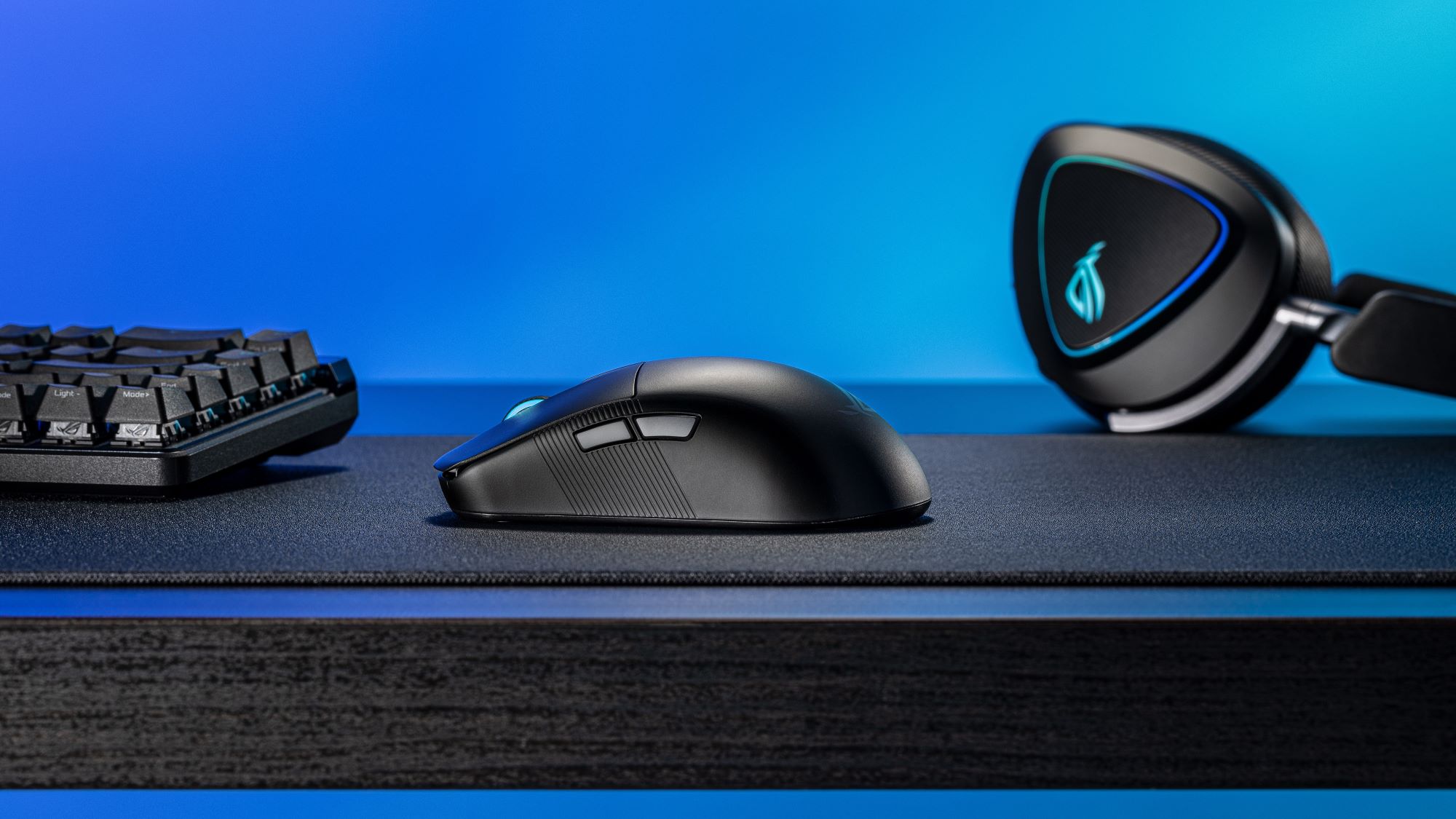 A side view of the ROG Harpe Ace Mini on a desk next to a keyboard and headset.