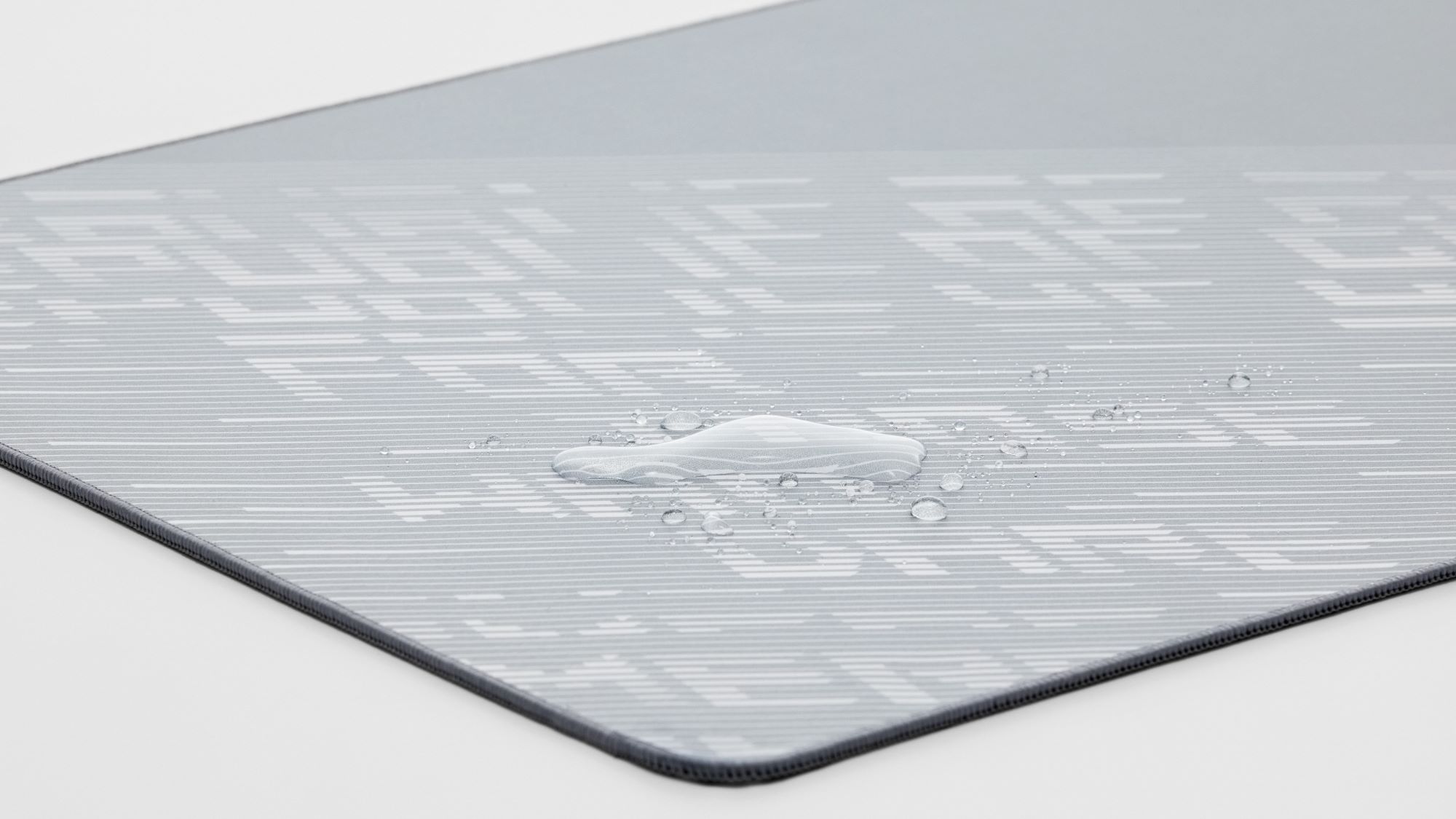 The ROG Scabbard II Arctic Gray XXL desk mat with a water spill resting atop its resistant surface.